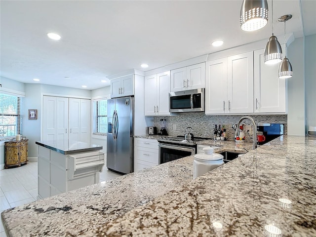 kitchen with appliances with stainless steel finishes, light stone counters, white cabinets, decorative light fixtures, and sink