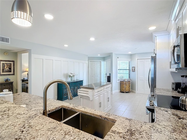 kitchen featuring fridge, sink, light stone counters, and white cabinets