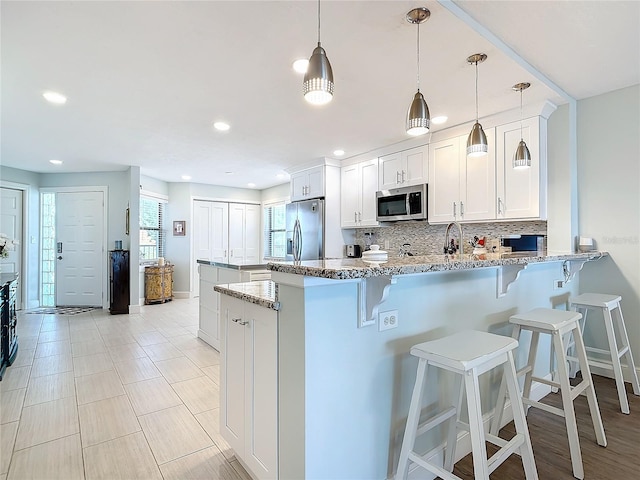 kitchen featuring white cabinets, stainless steel appliances, pendant lighting, and light stone countertops