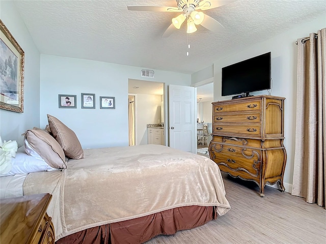 bedroom with a textured ceiling, connected bathroom, light wood-type flooring, and ceiling fan