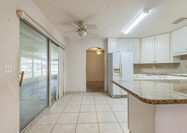 kitchen with a ceiling fan, light stone counters, white appliances, arched walkways, and white cabinetry