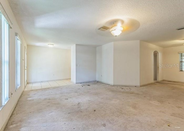 carpeted spare room with visible vents, a ceiling fan, arched walkways, baseboards, and a textured ceiling