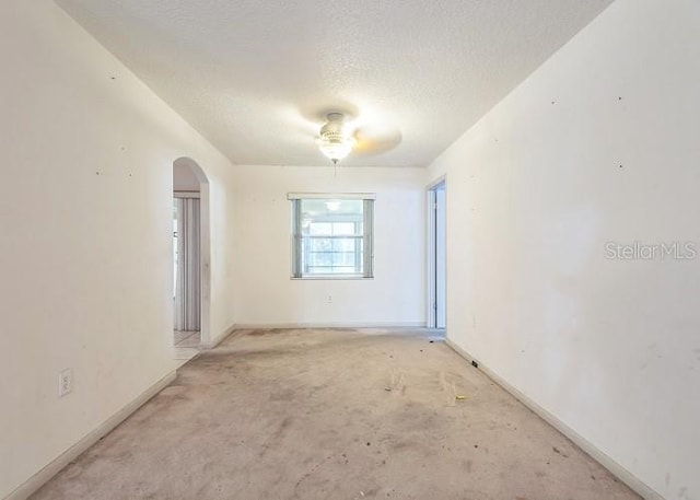 unfurnished room with arched walkways, a textured ceiling, and baseboards