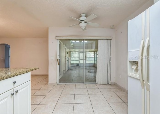 interior space with a textured ceiling, a ceiling fan, baseboards, and tile patterned floors