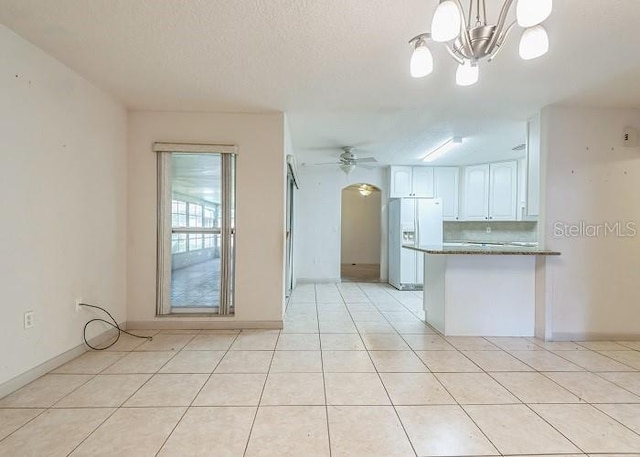 kitchen featuring light tile patterned floors, a peninsula, white refrigerator with ice dispenser, white cabinetry, and ceiling fan with notable chandelier