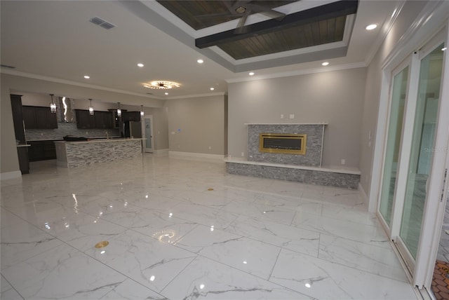 unfurnished living room featuring a high end fireplace, a tray ceiling, and crown molding