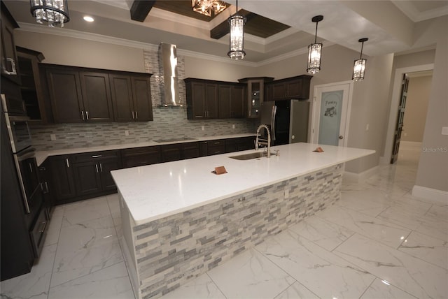 kitchen with stainless steel fridge, wall chimney range hood, a kitchen island with sink, and sink