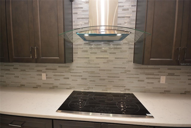 kitchen with island exhaust hood, dark brown cabinets, black stovetop, and backsplash