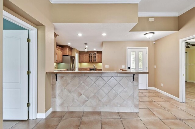 kitchen featuring light tile patterned floors, kitchen peninsula, stainless steel refrigerator, a breakfast bar, and crown molding