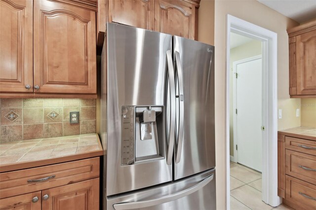 kitchen featuring light tile patterned flooring, decorative backsplash, stainless steel fridge, and tile counters