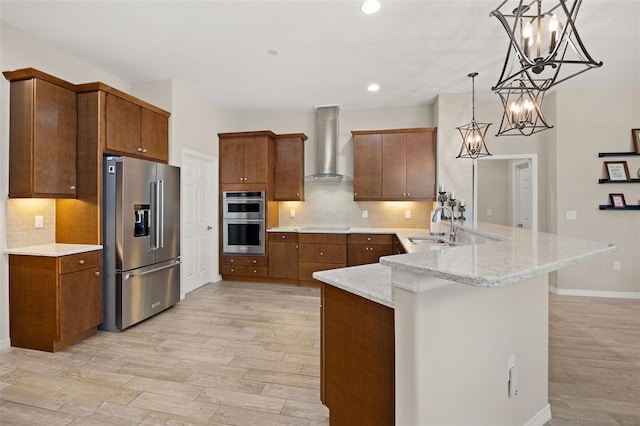 kitchen with light wood-type flooring, kitchen peninsula, wall chimney range hood, appliances with stainless steel finishes, and decorative light fixtures