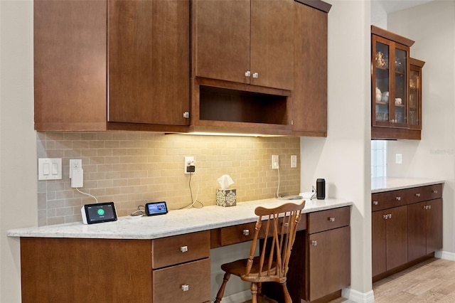 kitchen featuring built in desk, light wood-type flooring, light stone counters, and backsplash