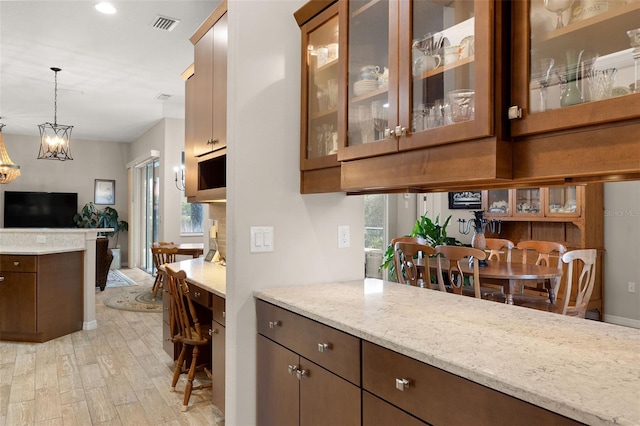 kitchen featuring light stone countertops, light wood-type flooring, an inviting chandelier, and decorative light fixtures