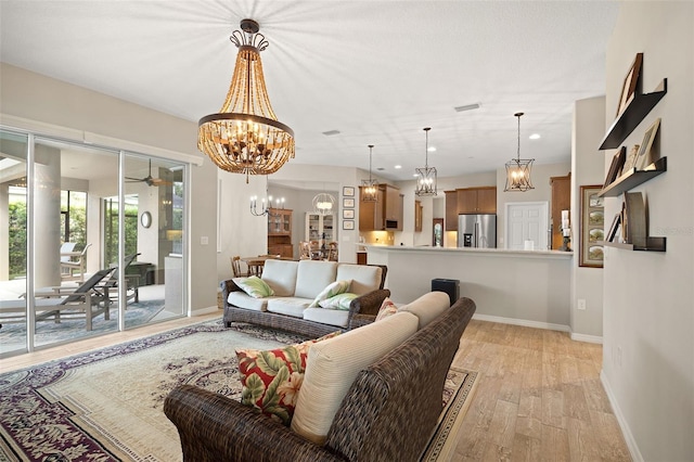 living room with ceiling fan with notable chandelier and light wood-type flooring