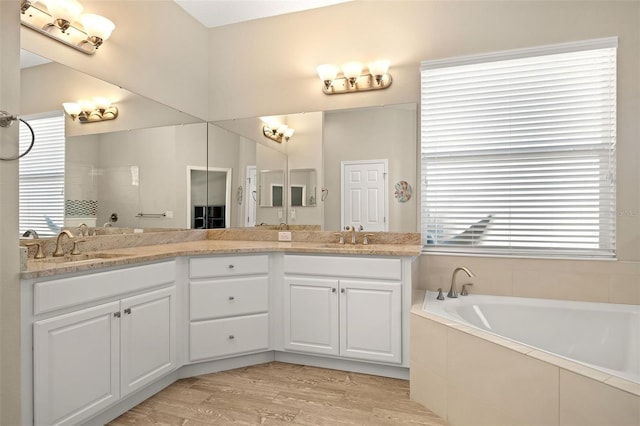 bathroom featuring wood-type flooring, tiled bath, and vanity