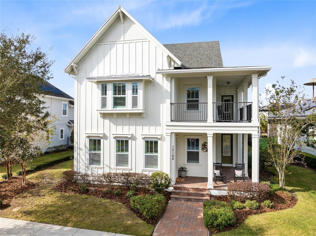 modern inspired farmhouse featuring a front yard, a porch, and a balcony