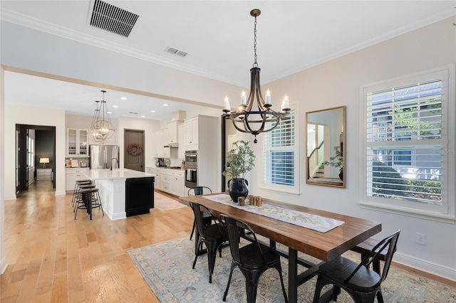 dining room with light hardwood / wood-style floors, sink, crown molding, and an inviting chandelier