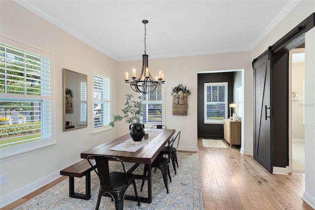 dining room featuring a barn door, light hardwood / wood-style flooring, a healthy amount of sunlight, and ornamental molding