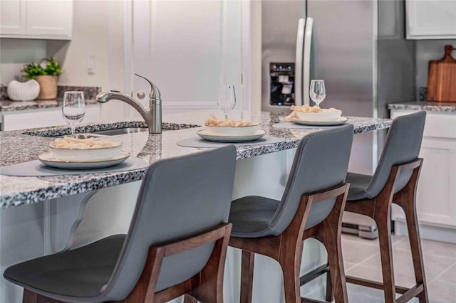 kitchen with stainless steel refrigerator with ice dispenser, light stone countertops, and white cabinetry