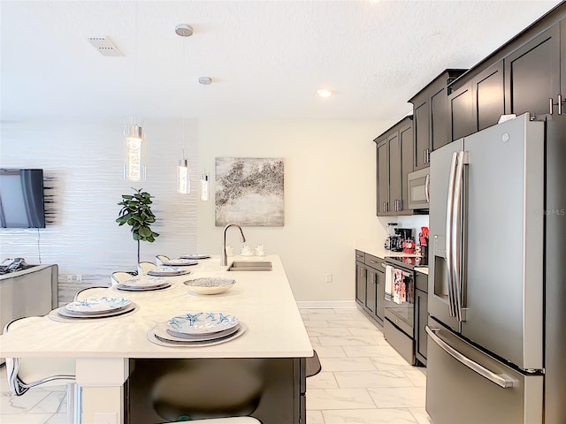 kitchen with an island with sink, sink, decorative light fixtures, appliances with stainless steel finishes, and a breakfast bar