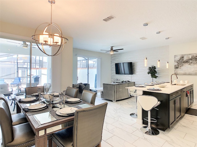 dining space with ceiling fan with notable chandelier and sink