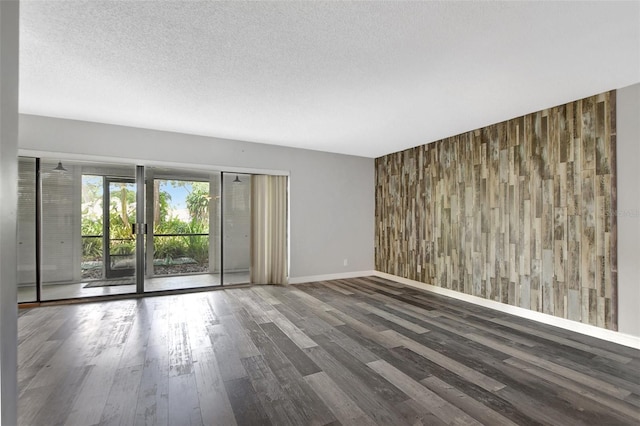 spare room featuring wood walls, an accent wall, a textured ceiling, and wood finished floors
