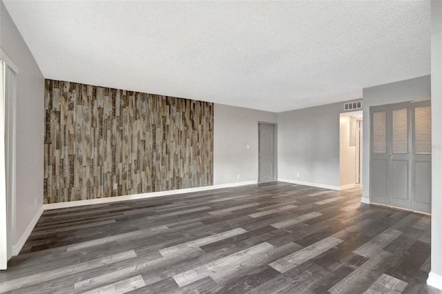 empty room with a textured ceiling, wooden walls, and dark hardwood / wood-style flooring