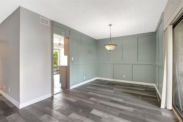 unfurnished dining area with baseboards, dark wood-style floors, a textured ceiling, visible vents, and a decorative wall