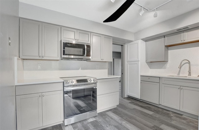 kitchen featuring sink, rail lighting, gray cabinetry, appliances with stainless steel finishes, and hardwood / wood-style floors