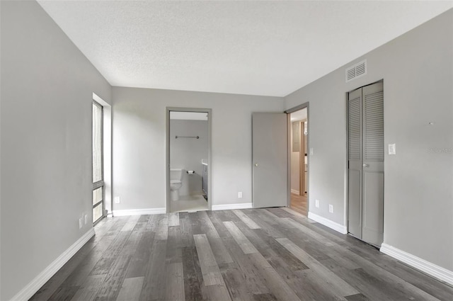 unfurnished bedroom with multiple windows, a textured ceiling, connected bathroom, and dark hardwood / wood-style flooring