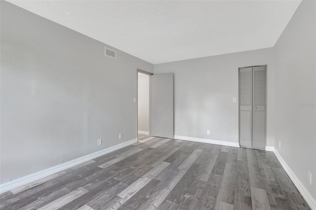 empty room with visible vents, baseboards, a textured ceiling, and wood finished floors