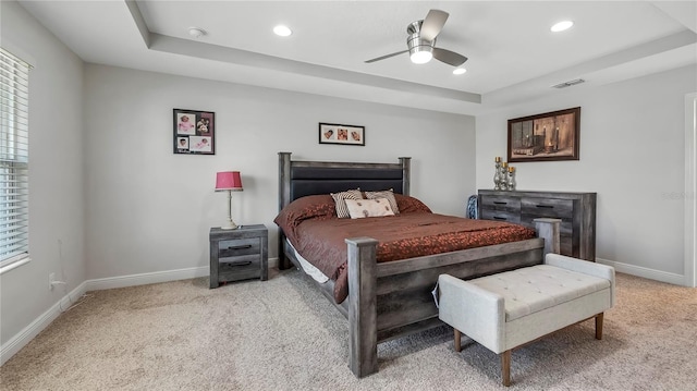 bedroom with light colored carpet, a tray ceiling, and ceiling fan