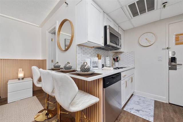 kitchen featuring white cabinets, appliances with stainless steel finishes, a breakfast bar, dark hardwood / wood-style flooring, and decorative backsplash