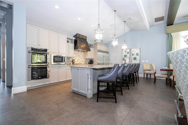 kitchen featuring premium range hood, a center island with sink, white cabinetry, built in appliances, and lofted ceiling with beams