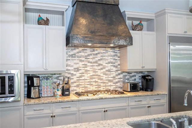 kitchen featuring built in appliances, custom range hood, decorative backsplash, and white cabinetry