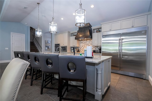 kitchen with hanging light fixtures, white cabinetry, built in appliances, lofted ceiling, and a center island with sink