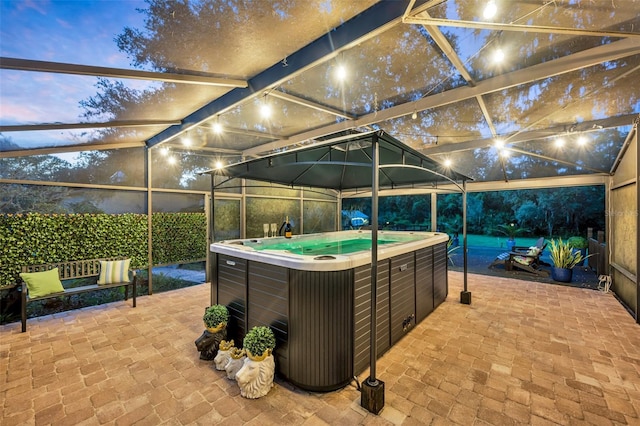 patio terrace at dusk featuring a lanai and a hot tub