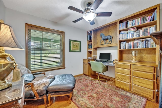 office space featuring a textured ceiling, ceiling fan, built in desk, and hardwood / wood-style flooring