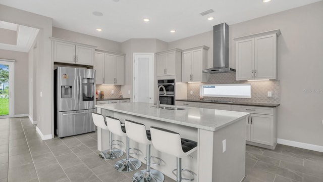 kitchen featuring tasteful backsplash, a center island with sink, wall chimney exhaust hood, appliances with stainless steel finishes, and a breakfast bar area