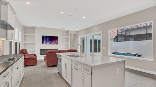 kitchen with a center island with sink, white cabinetry, black electric stovetop, built in shelves, and sink