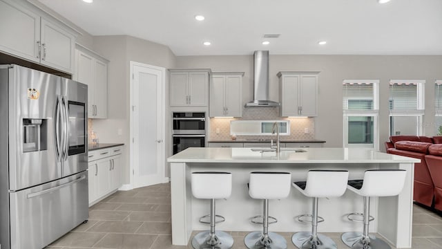 kitchen with a kitchen island with sink, stainless steel appliances, wall chimney exhaust hood, and a kitchen breakfast bar