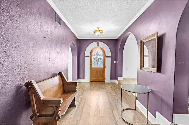 foyer entrance featuring a textured ceiling, light wood-type flooring, and ornamental molding