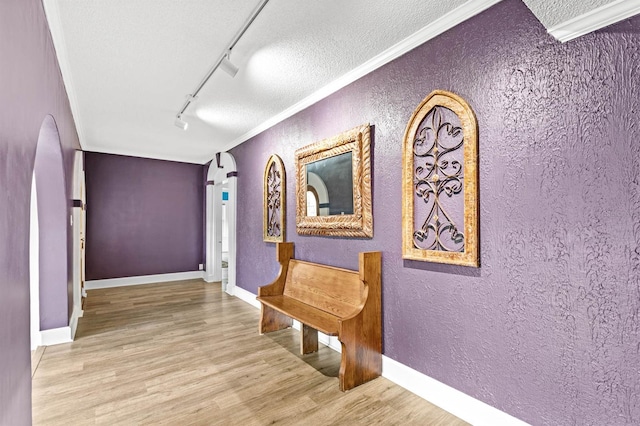 hallway with a textured ceiling, rail lighting, hardwood / wood-style flooring, and crown molding