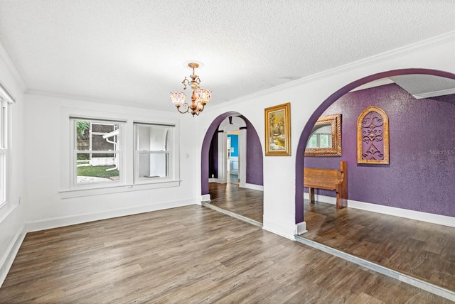 unfurnished dining area featuring wood-type flooring, a textured ceiling, crown molding, and a notable chandelier