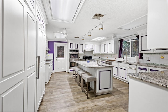 kitchen with a center island, a kitchen bar, light stone countertops, black range with electric stovetop, and light hardwood / wood-style flooring