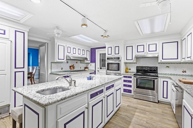 kitchen featuring stainless steel appliances, backsplash, light wood-type flooring, sink, and a kitchen island with sink