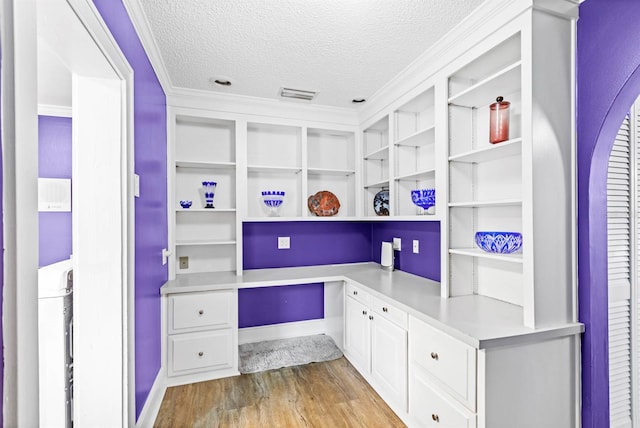 office with light wood-type flooring, a textured ceiling, built in desk, and crown molding