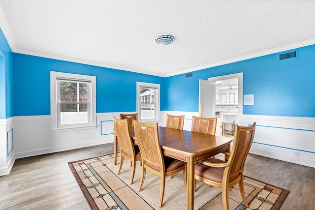 dining area featuring light hardwood / wood-style floors, a textured ceiling, and crown molding