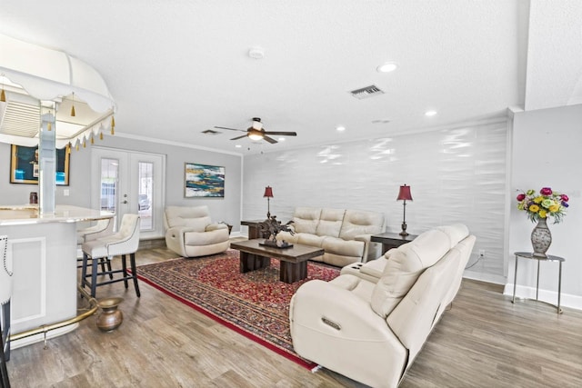 living room featuring ornamental molding, ceiling fan, a textured ceiling, hardwood / wood-style floors, and french doors