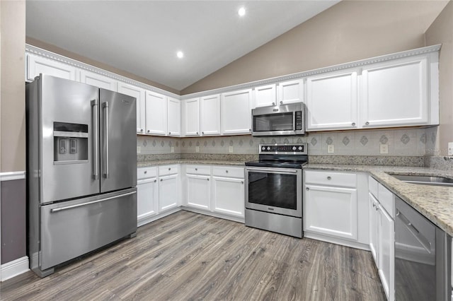 kitchen with vaulted ceiling, light stone countertops, white cabinets, and appliances with stainless steel finishes